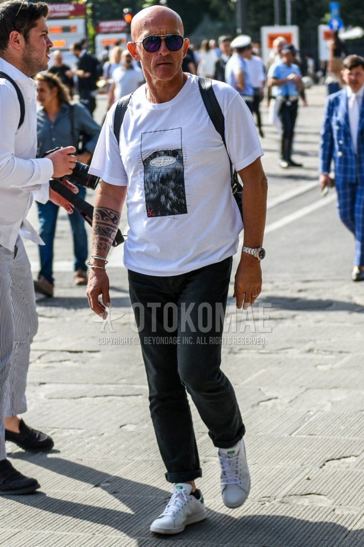 シルバー無地のサングラス、白グラフィックのTシャツ、ダークグレー無地のコットンパンツ、アディダス　スタンスミスの白ローカットのスニーカーを合わせた夏のメンズコーデ・着こなし。