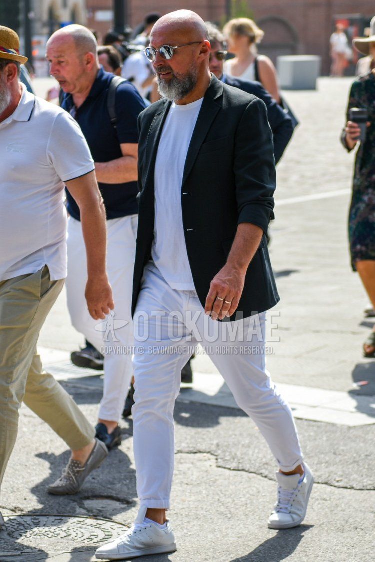 Spring and fall men's coordinate and outfit with clear plain sunglasses, plain black tailored jacket, plain white t-shirt, plain white cotton pants, and white low-cut Adidas Stan Smith sneakers.
