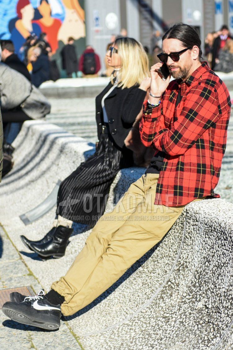 Men's spring/fall/winter outfit with plain black sunglasses, red/black checked shirt, plain beige chinos, plain black socks, and black low-cut Nike sneakers.