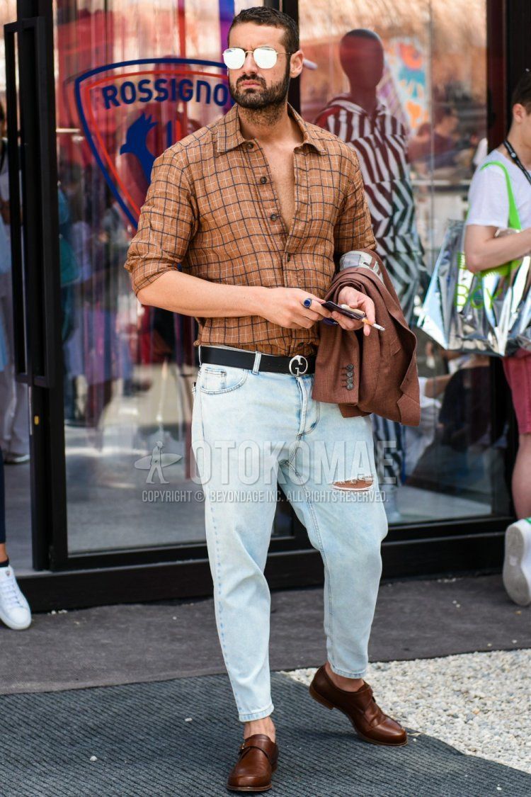 Men's spring/summer coordinate and outfit with plain gold/silver sunglasses, brown checked shirt, plain black leather belt, plain light blue damaged jeans, and brown monk shoe leather shoes.