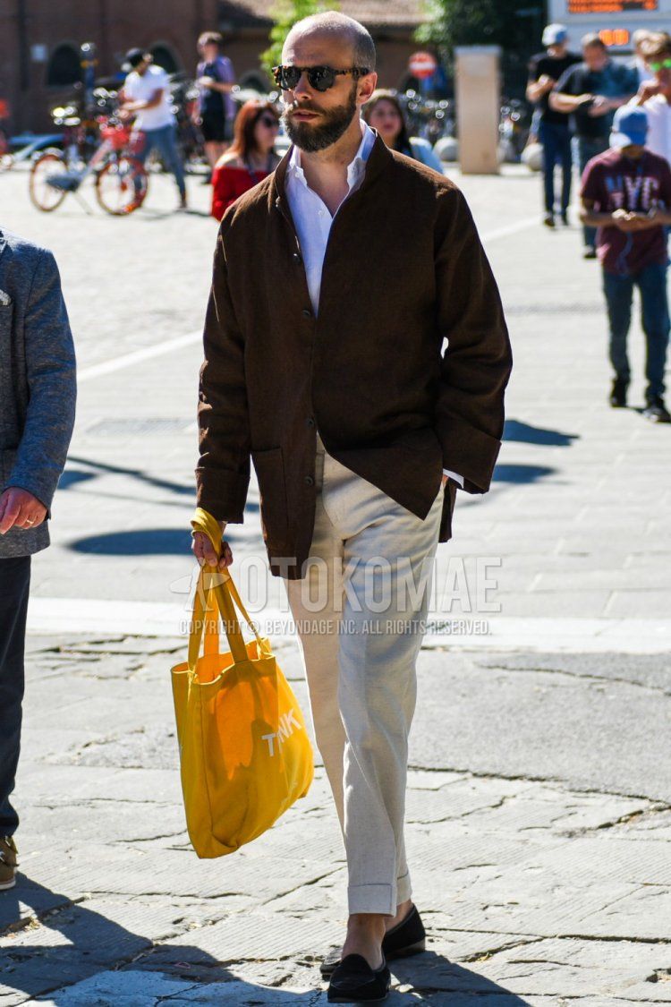 Men's spring and fall outfit with brown tortoiseshell sunglasses, plain brown tailored jacket, plain white linen shirt, plain beige beltless pants, plain slacks, suede brown coin loafer leather shoes, yellow graphic tote bag.