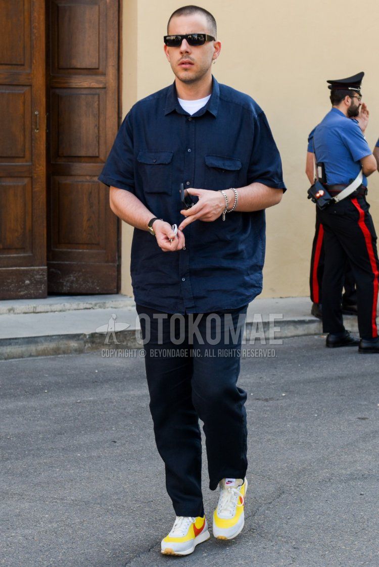 Summer men's coordinate and outfit with plain black sunglasses, plain navy shirt jacket, plain white t-shirt, plain navy cotton pants, and Nike yellow low-cut sneakers.