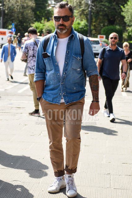 Men's spring, summer, and fall coordinate and outfit with solid black sunglasses, solid blue denim/chambray shirt, solid white t-shirt, solid beige cotton pants, and Stan Smith white low-cut sneakers.