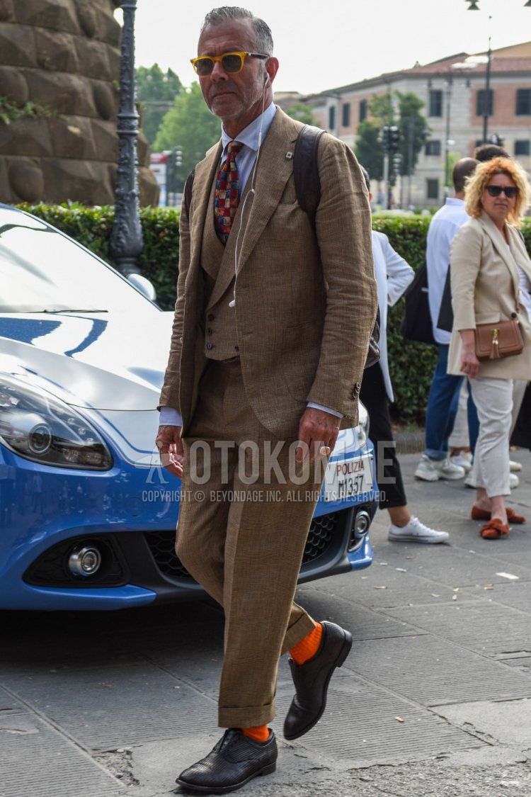 Men's spring and fall outfit with solid orange-brown sunglasses, solid white shirt, solid orange socks, black straight-tip leather shoes, solid beige-brown three-piece suit, and solid multi-colored tie.