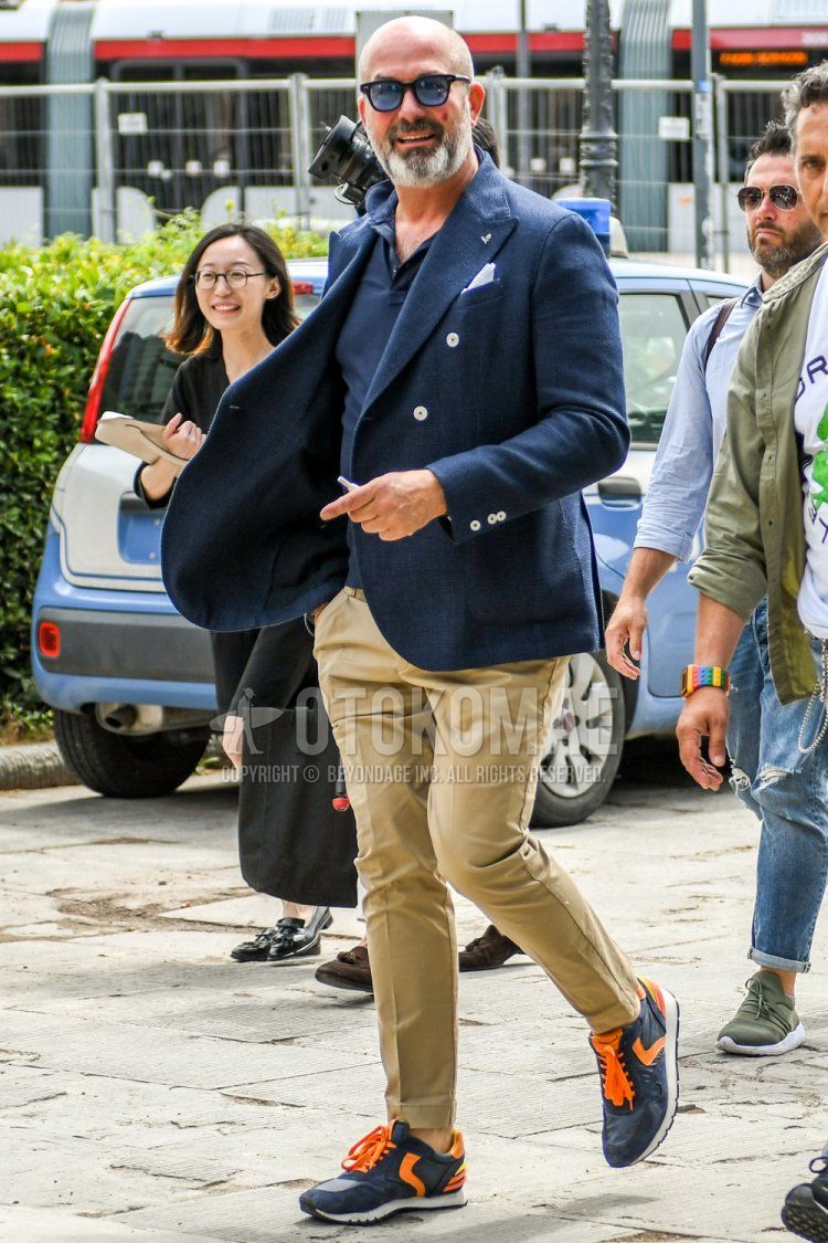 Men's spring/summer coordinate and outfit with plain black sunglasses, plain navy tailored jacket, plain navy polo shirt, plain beige chinos, and navy/orange low-cut sneakers by Boyle Blanche.