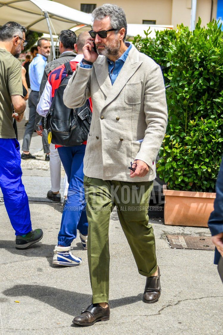 Men's spring, summer, and fall coordinate and outfit with solid color sunglasses, solid color beige tailored jacket, solid color blue denim/chambray shirt, solid color olive green slacks, and brown monk shoe leather shoes.