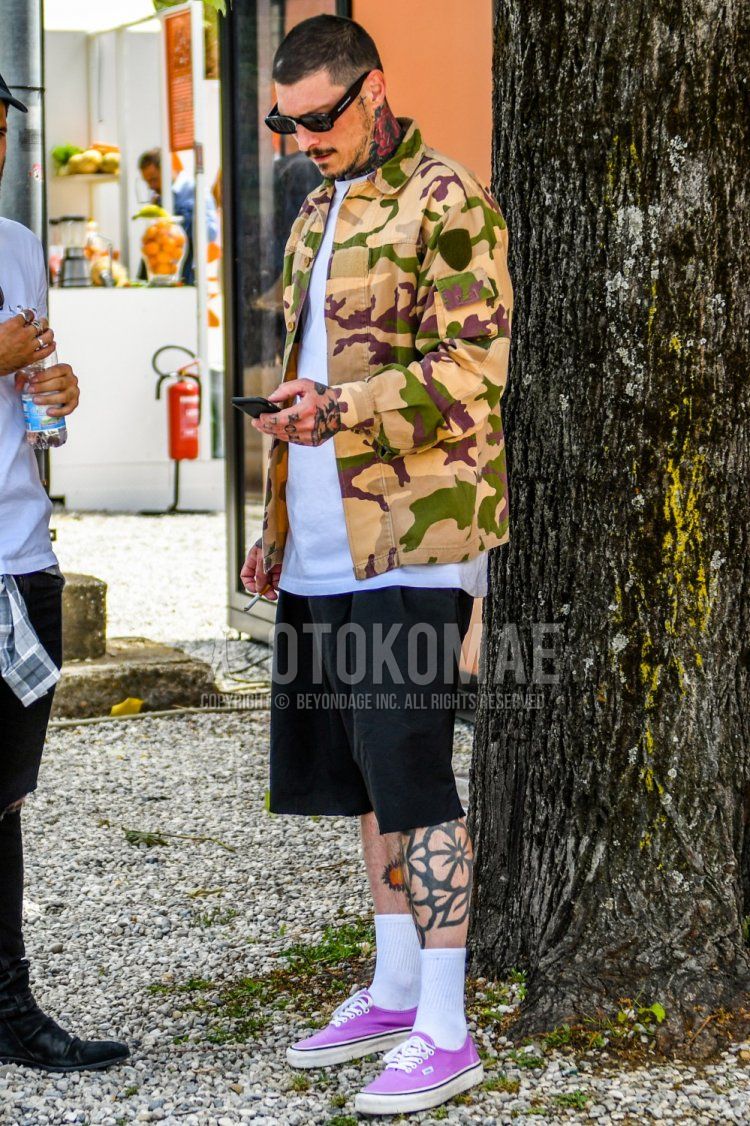 黒無地のサングラス、ベージュ・グリーン迷彩のシャツジャケット、白無地のTシャツ、黒無地のショートパンツ、白無地のソックス、パープルローカットのスニーカーを合わせた春夏秋のメンズコーデ・着こなし。
