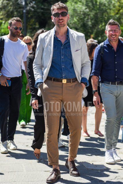 Men's spring/fall outfit with plain black sunglasses, white striped tailored jacket, plain blue denim/chambray shirt, Louis Vuitton brown leather belt, plain beige chinos, and brown plain toe leather shoes.