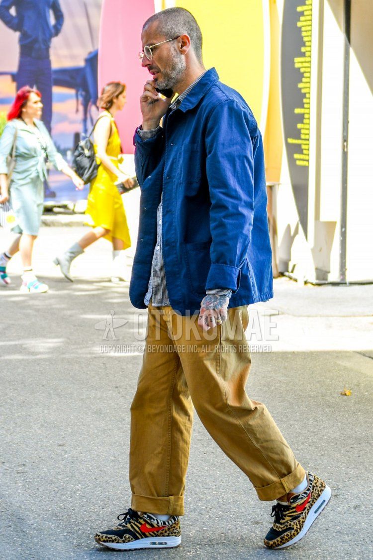 Men's spring, summer, and fall coordinate and outfit with plain silver glasses, plain blue shirt jacket, blue striped shirt, plain beige chinos, plain white socks, and Nike Atmos Air Max 180 beige low-cut sneakers.