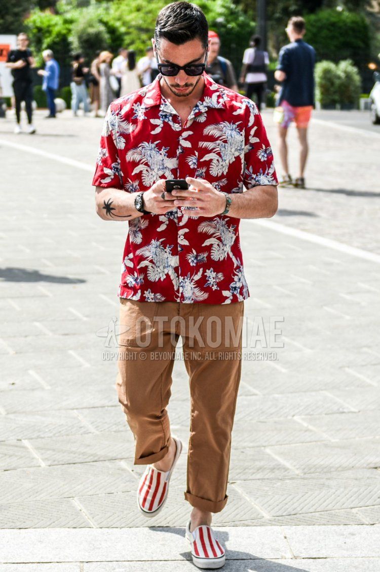 Summer men's coordinate and outfit with plain black sunglasses, short sleeve open collar red botanical shirt, plain beige/brown cargo pants, and white/red slip-on sneakers.