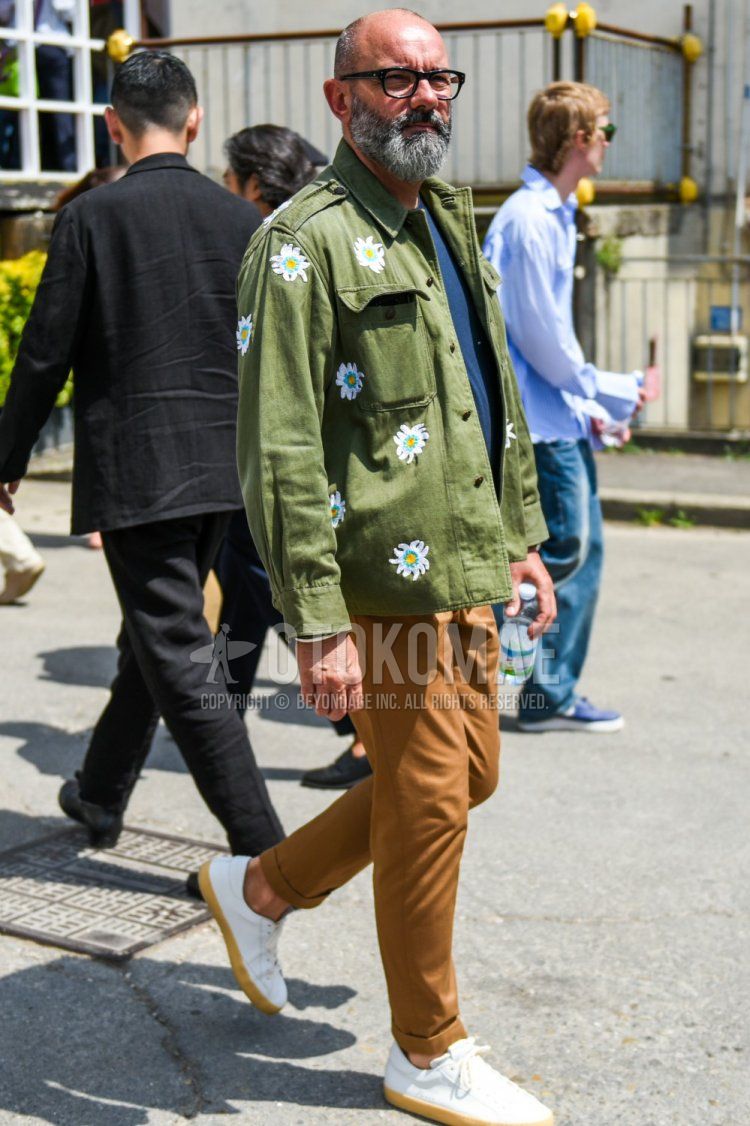 Men's spring and fall coordinate and outfit with plain black glasses, plain olive green shirt jacket, plain navy t-shirt, plain brown slacks, and white low-cut sneakers.