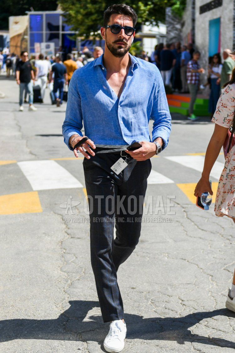 Men's summer coordinate and outfit with plain navy sunglasses from Boston, plain light blue linen shirt, dark gray checked slacks, and white low-cut sneakers.