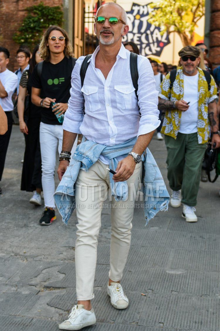 Men's summer coordinate and outfit with brown tortoiseshell sunglasses, linen plain white shirt, beige plain denisla, and white low-cut sneakers.