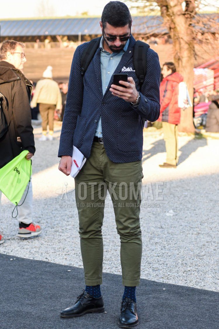 Men's spring/fall outfit with brown tortoiseshell sunglasses, navy-dot tailored jacket, solid light blue denim/chambray shirt, solid black leather belt, solid olive green chinos, navy socks, black plain-toe leather shoes.