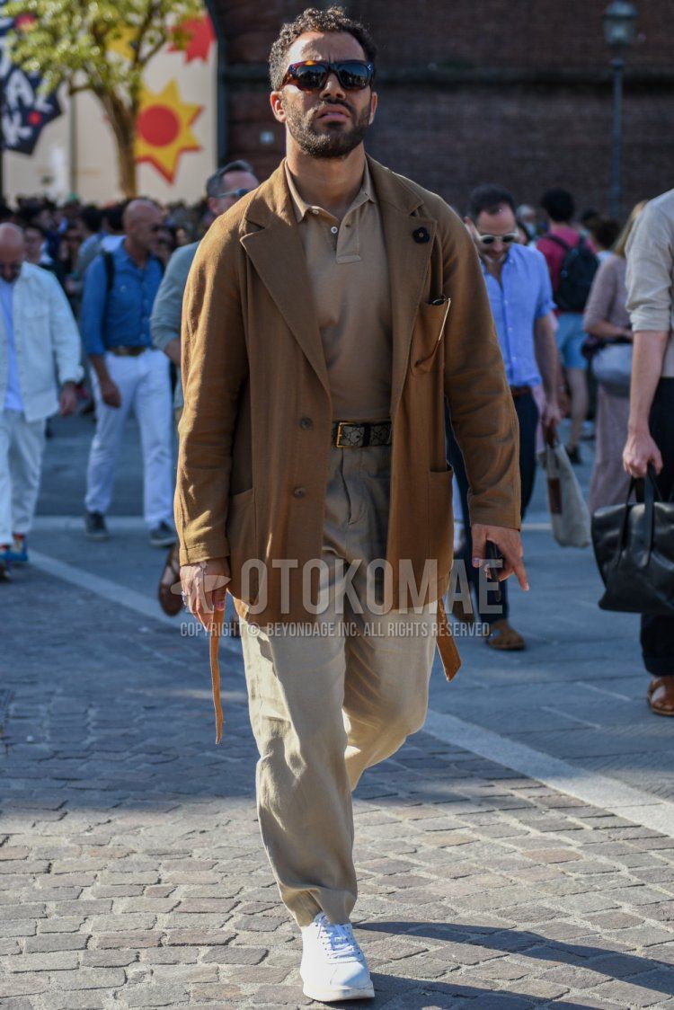 Men's spring/summer coordinate and outfit with brown tortoiseshell sunglasses, plain beige tailored jacket by Lardini, plain beige polo shirt, beige leather belt, plain beige chinos and white low-cut sneakers.