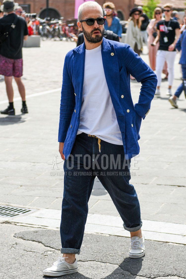 Men's spring/summer/fall outfit with plain black sunglasses, plain navy tailored jacket, plain white t-shirt, plain beige mesh belt, plain navy denim/jeans, and white low-cut sneakers by Vans.