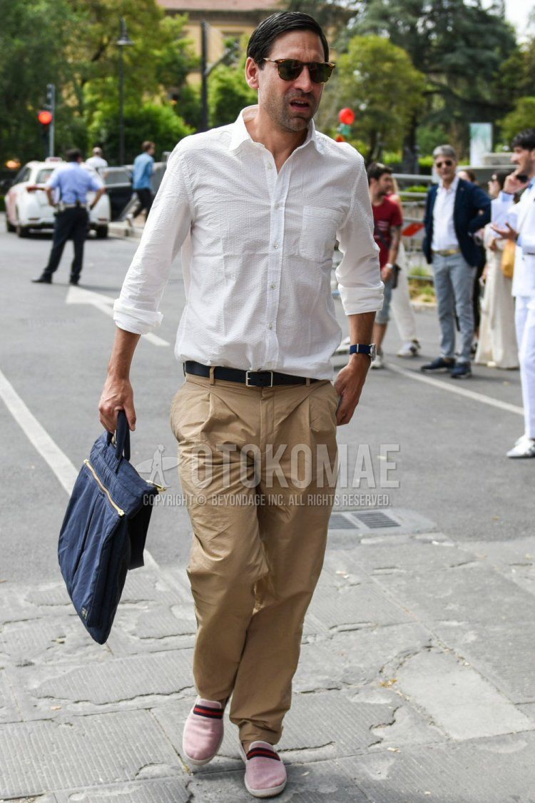 Men's spring/summer coordinate and outfit with brown tortoiseshell sunglasses, plain white shirt, plain black leather belt, plain beige chinos, pink slip-on sneakers, and plain navy briefcase/handbag.