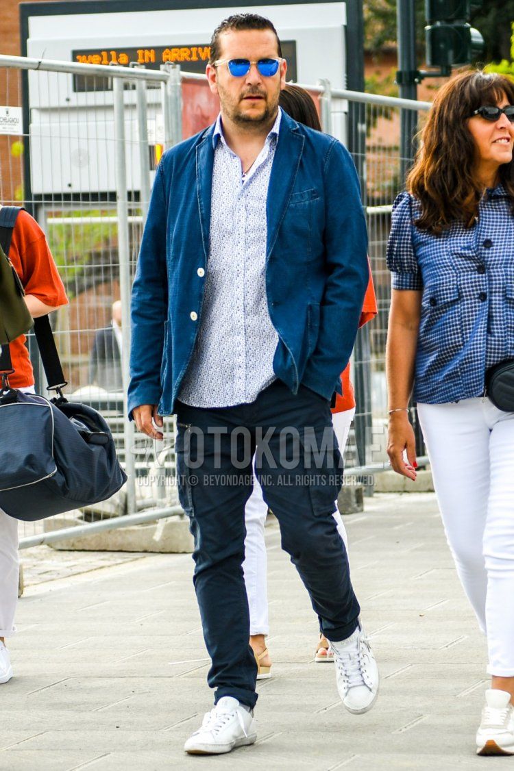 Men's spring, summer, and fall coordinate and outfit with solid color sunglasses, solid color blue tailored jacket, white top/inner shirt, solid color navy cargo pants, solid color navy cotton pants, and white low-cut sneakers.