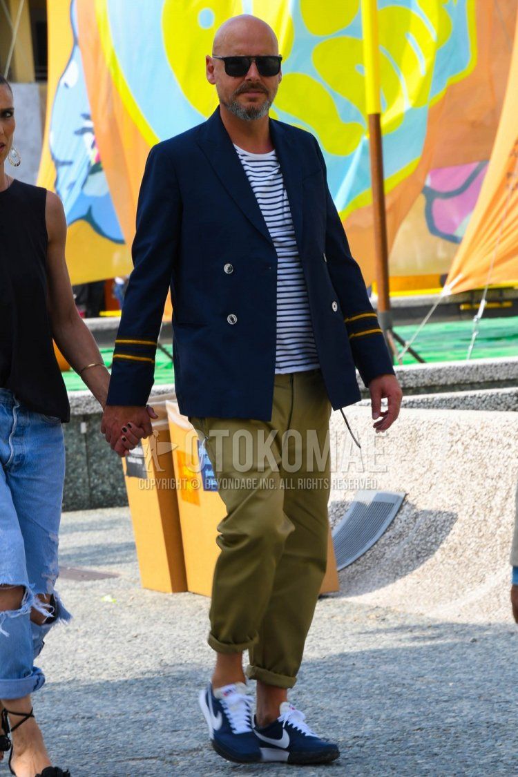 Men's spring, summer, and fall coordinate and outfit with plain sunglasses, plain navy tailored jacket, white and black striped t-shirt, plain beige chinos, and Nike blue low-cut sneakers.