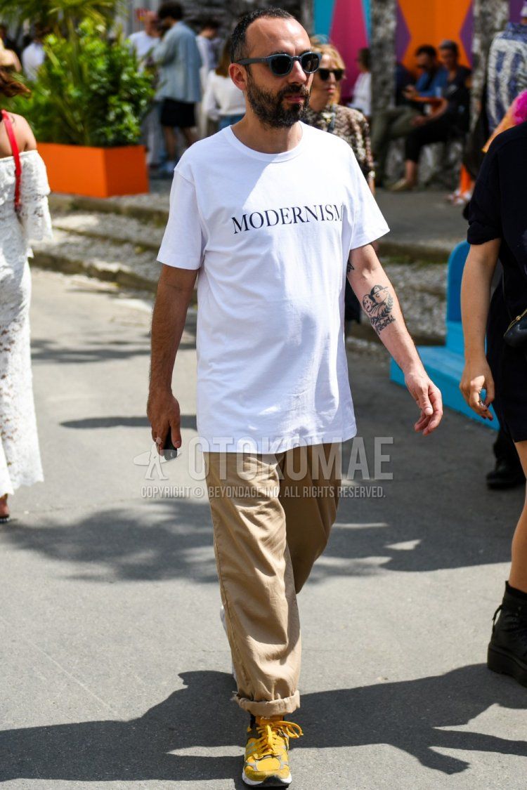 Men's summer coordinate and outfit with dark gray solid color sunglasses, white graphic t-shirt, beige solid color wide pants, and yellow low-cut sneakers.
