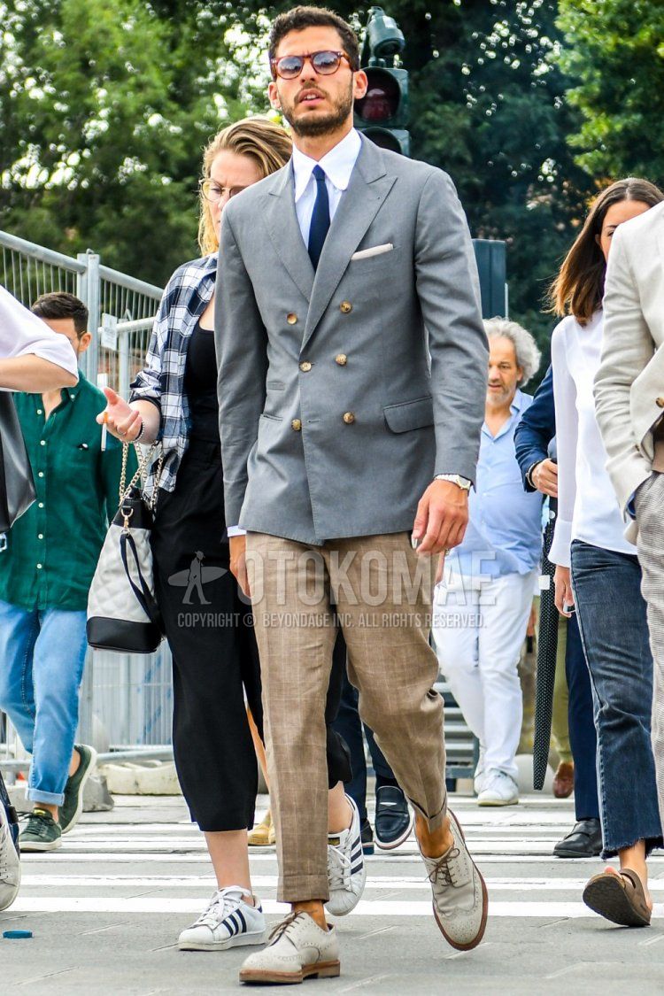 Men's spring/summer/fall outfit with brown tortoiseshell sunglasses, plain gray tailored jacket, plain white shirt, beige checked slacks, gray brogue shoes leather shoes, and plain blue tie.