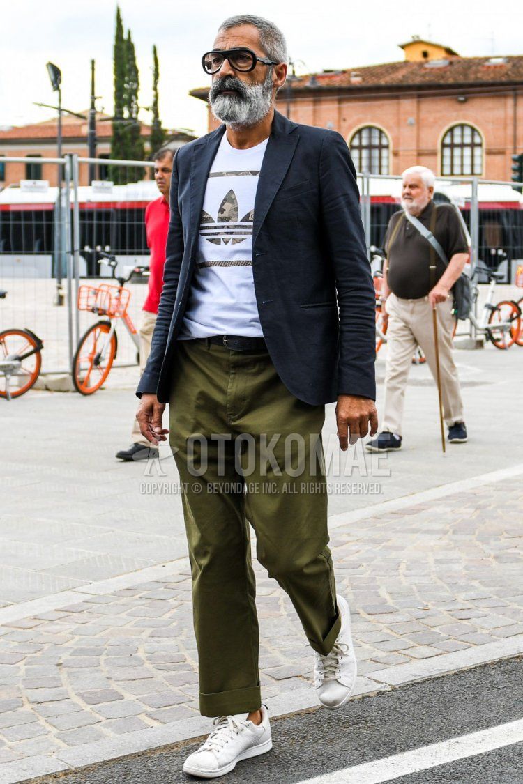 Men's spring, summer, and fall coordinate and outfit with plain glasses, plain navy tailored jacket, Adidas t-shirt with white decal logo, plain black leather belt, olive green plain wide-leg pants, and white low-cut sneakers.