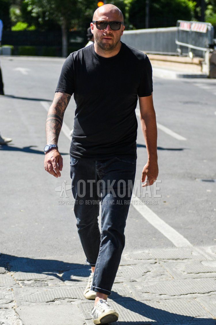 Men's summer coordinate and outfit with brown tortoiseshell sunglasses, plain black t-shirt, dark gray plain denisla, and white low-cut sneakers.