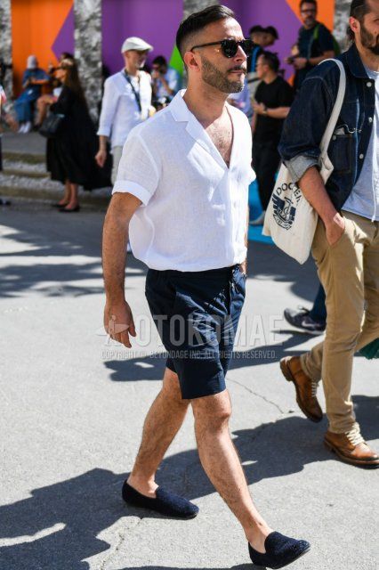 Men's summer coordinate and outfit with Boston plain black sunglasses, open collar linen plain white shirt, plain navy shorts, and navy loafer leather shoes.