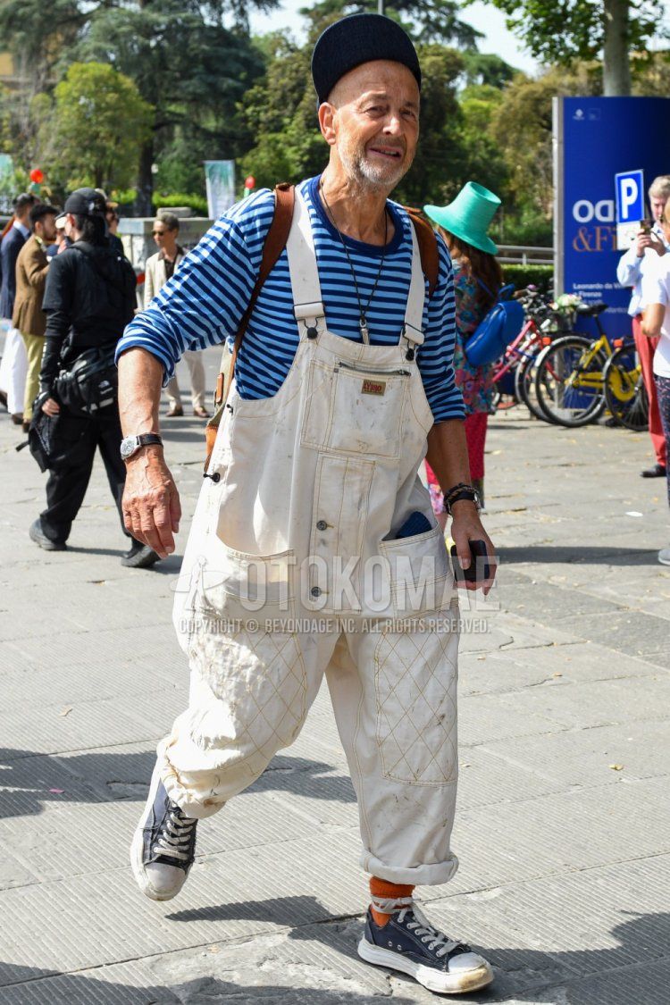 Men's spring, summer, and fall coordinate and outfit with plain navy cap, overall plain white jumpsuit, blue/light blue striped long T, plain orange socks, and navy low-cut sneakers.