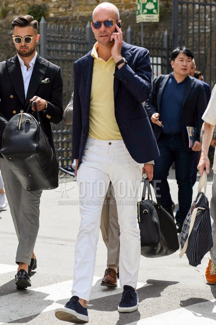Men's spring/summer/fall coordinate and outfit with brown tortoiseshell sunglasses, plain navy tailored jacket, plain yellow polo shirt, plain white denim/jeans, and navy low-cut sneakers.