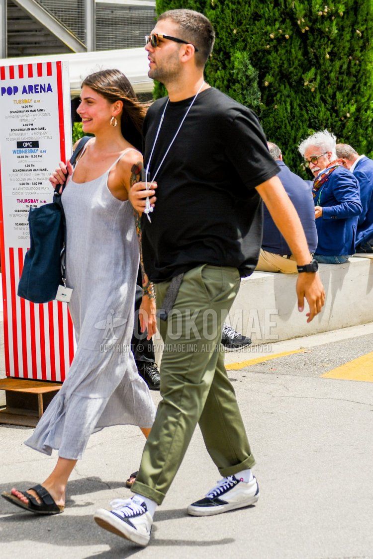 Men's summer coordinate and outfit with plain sunglasses, plain black t-shirt, plain green chinos, plain white socks, and white/black low-cut sneakers.