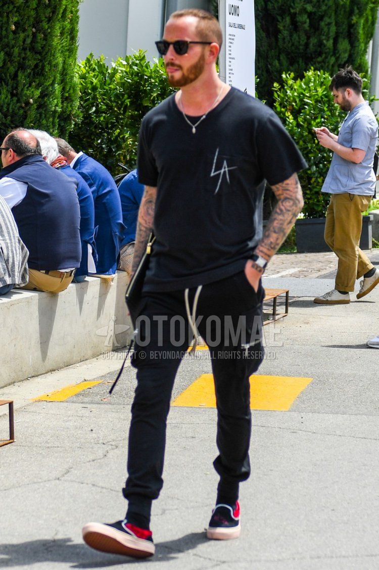 A summer men's coordinate and outfit with plain sunglasses, black lettered t-shirt, plain black cargo pants, plain jogger pants/ribbed pants, and slip-on sneakers.