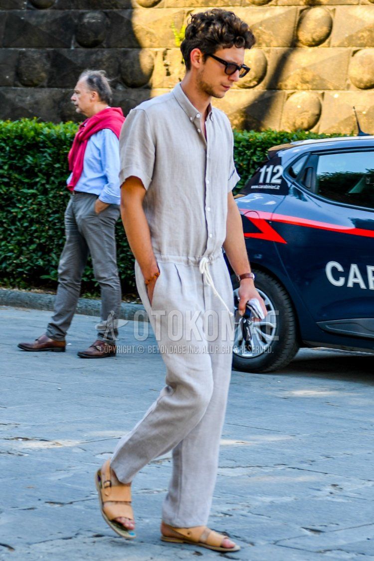A summer men's coordinate and outfit with solid color sunglasses, solid color beige shirt, solid color beige easy pants, and orange leather sandals.