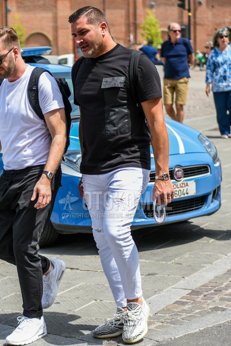 Men's summer coordinate and outfit with plain black t-shirt, plain white denim/jeans, and Adidas Yeezy Boost white and black low-cut sneakers.