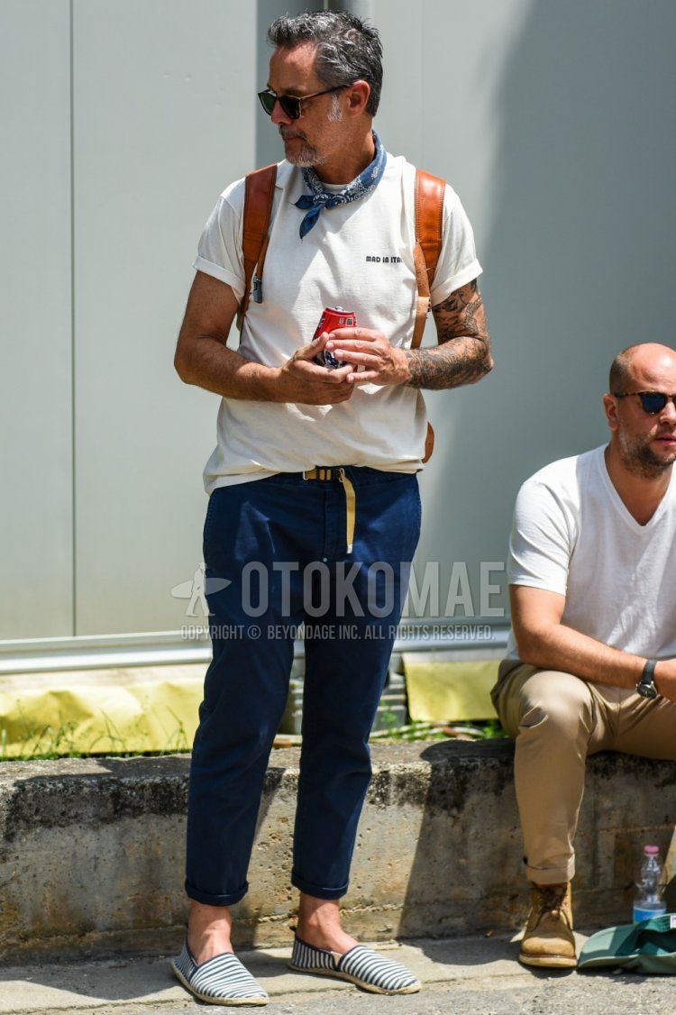 ブラウンべっ甲のサングラス、ネイビーペイズリーのバンダナ/ネッカチーフ、白ワンポイントのTシャツ、ベージュ無地のテープベルト、ネイビー無地のクロップドパンツ、無地のチノパン、ネイビー・白ストライプのエスパドリーユを合わせた夏のメンズコーデ・着こなし。