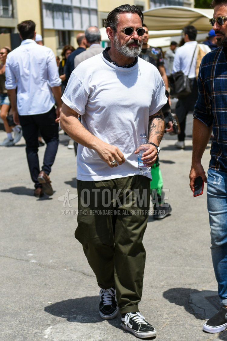 Summer men's coordinate and outfit with round black and silver plain sunglasses, black stole bandana/neckerchief, plain white t-shirt, olive green plain chinos, and black high-cut sneakers from Vans Skehai.