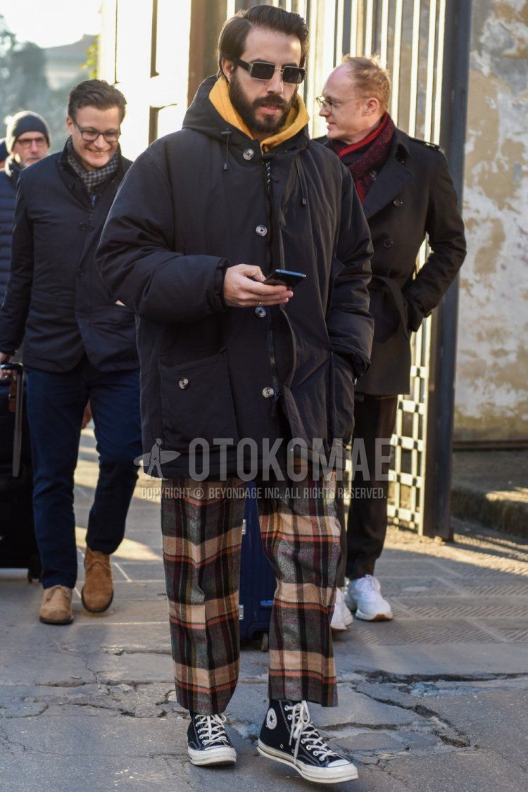 Winter men's coordinate and outfit with plain black sunglasses, plain black hooded coat, multi-colored checked slacks, and Converse Chuck Taylor black high-cut sneakers.