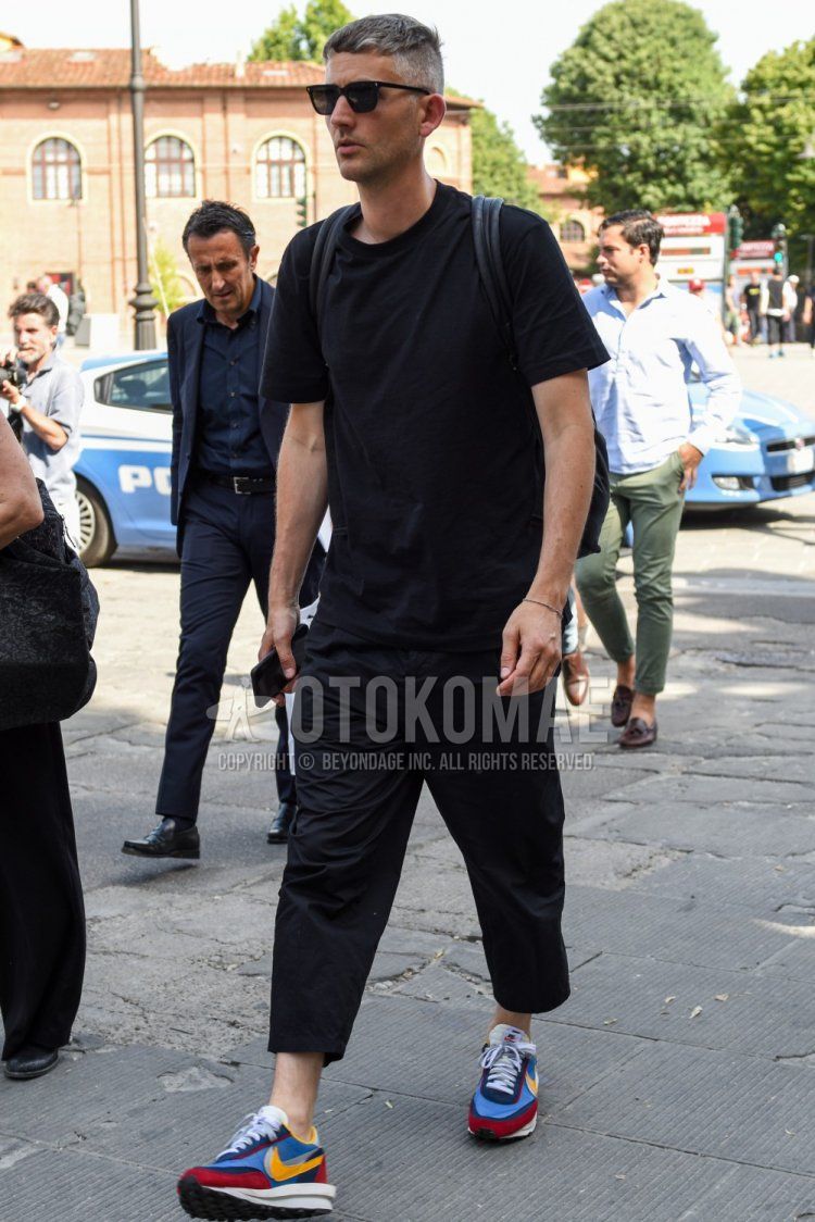 Summer men's coordinate and outfit with plain black sunglasses, plain black t-shirt, plain black cropped pants, and Nike Sakai multi-colored low-cut sneakers.