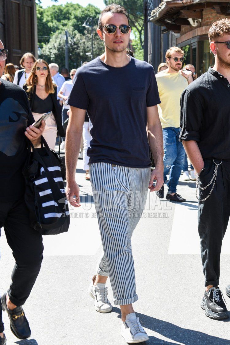 A summer men's coordinate and outfit with plain black sunglasses, plain navy t-shirt, white/blue striped slacks, and white low-cut sneakers.