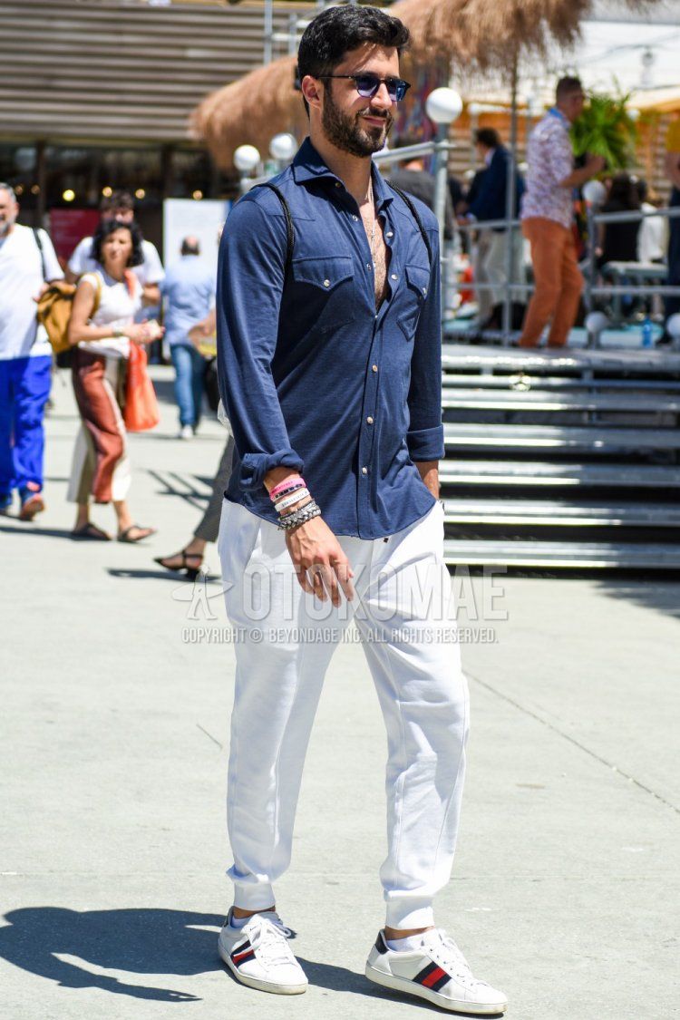 Men's spring/summer coordinate and outfit with black tortoiseshell sunglasses, plain navy shirt, plain white cotton pants, and white low-cut Gucci sneakers.