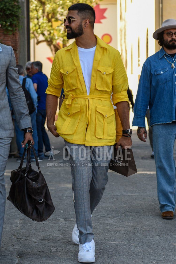 Men's spring, summer, and fall coordinate and outfit with gold and black plain sunglasses, yellow plain safari jacket, white plain t-shirt, gray checked slacks, and white low-cut sneakers.