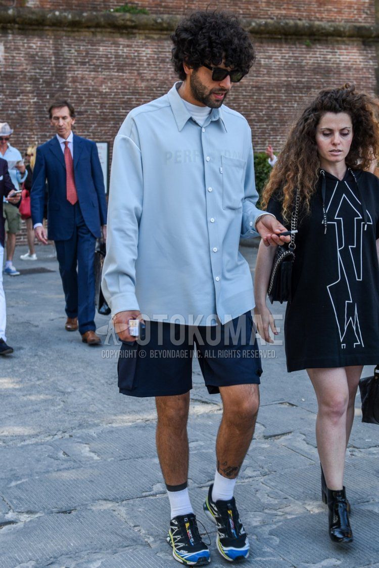 Men's spring, summer, and fall coordinate and outfit with Wellington solid black sunglasses, solid light blue shirt, solid navy shorts, solid white socks, and multi-colored low-cut sneakers.