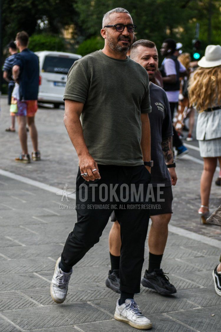 Summer men's coordinate and outfit with plain black glasses, plain olive green t-shirt, plain black denim/jeans, plain black socks, and Nike Air Force 1 white low-cut sneakers.