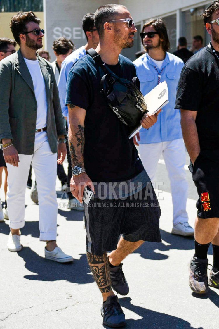 Summer men's coordinate and outfit with clear solid color sunglasses, solid color black t-shirt, solid color gray t-shirt, black bottom sideline pants, bottom shorts, dark gray low cut sneakers, and black solid color Supreme shoulder bag.