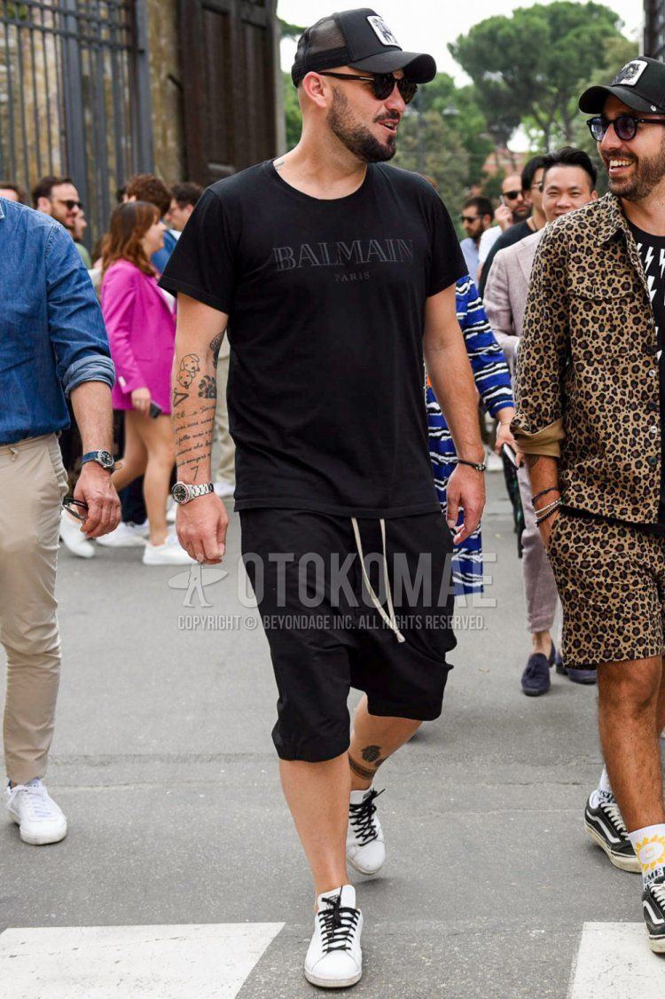 Summer men's coordinate and outfit with black one-pointed baseball cap, solid black sunglasses, solid black t-shirt, solid black easy pants, solid black shorts, and low-cut sneakers.