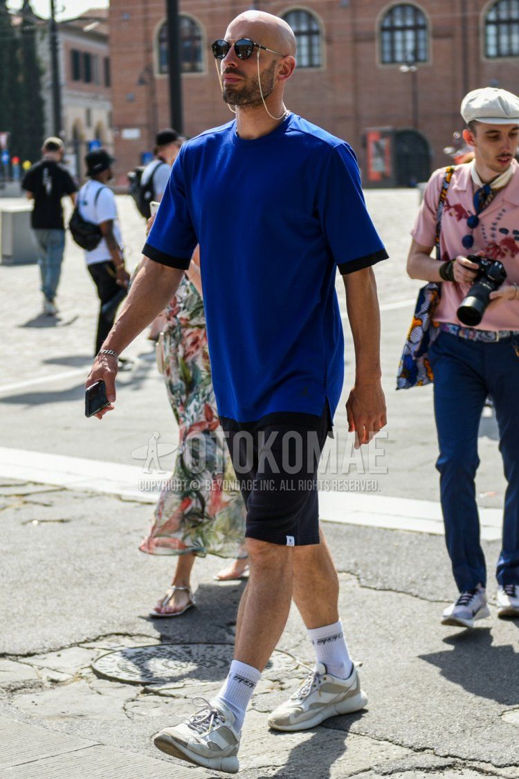 Men's summer coordinate and outfit with plain black sunglasses, plain blue t-shirt, plain black shorts, plain white socks, and white low-cut sneakers.