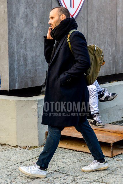 Men's fall/winter outfit with solid black scarf/stall, solid black chester coat, solid black/gray denim/jeans, solid black socks, Reebok white low-cut sneakers, and solid olive green backpack.