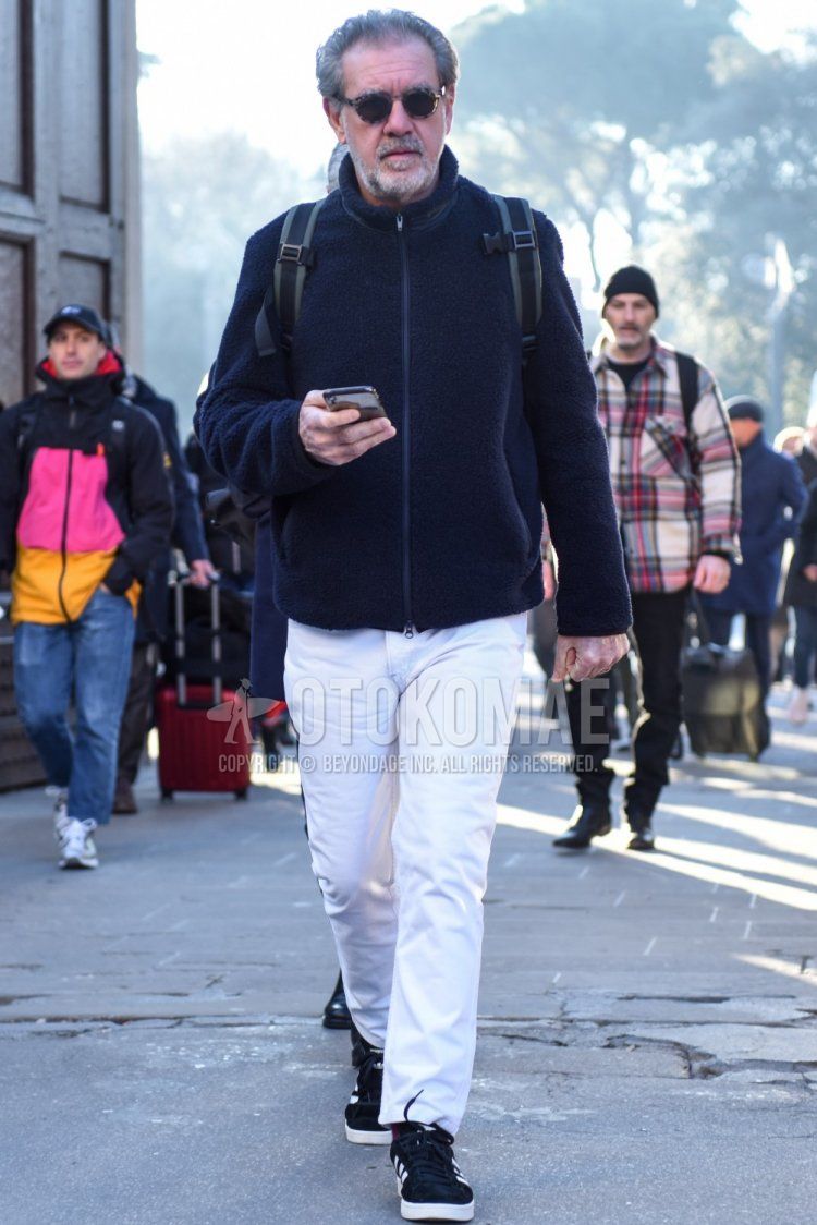 Men's fall/winter coordinate and outfit with dark gray tortoiseshell sunglasses, plain black fleece jacket, plain white cotton pants, plain white ankle pants, and Adidas Campus black low-cut sneakers.