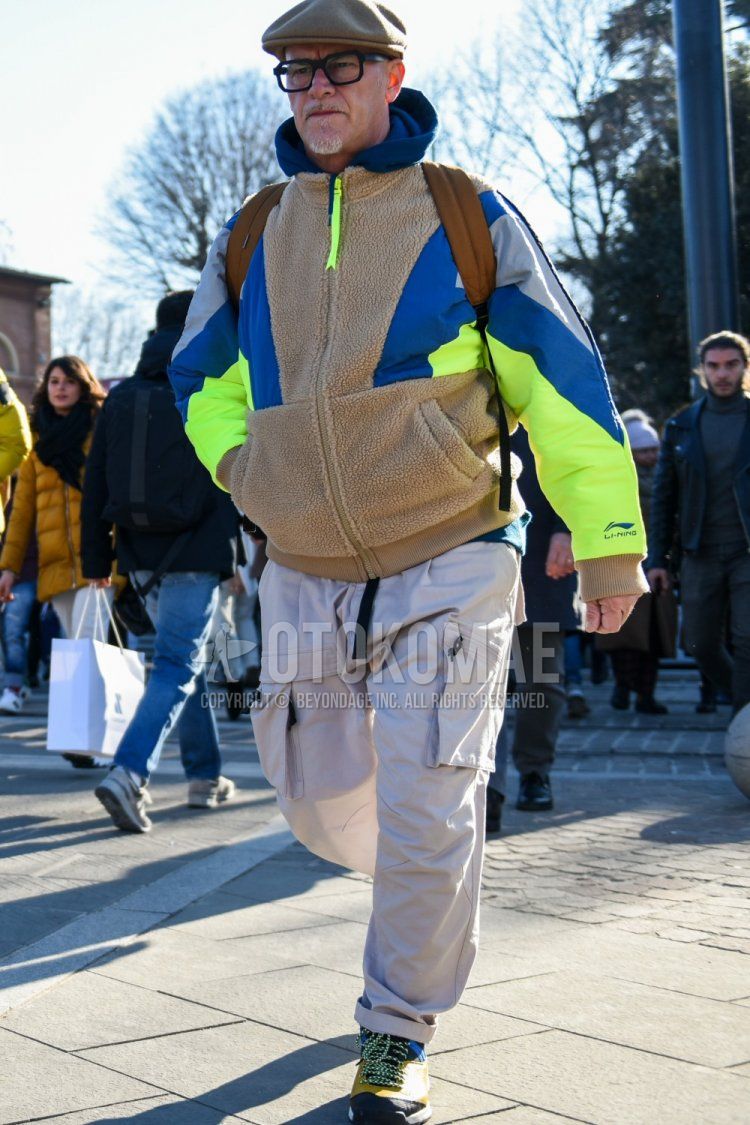 Men's fall/winter coordinate and outfit with solid beige hunting cap, solid black glasses, solid beige fleece jacket, solid blue hoodie, solid white cargo pants, and yellow/blue high-cut sneakers.