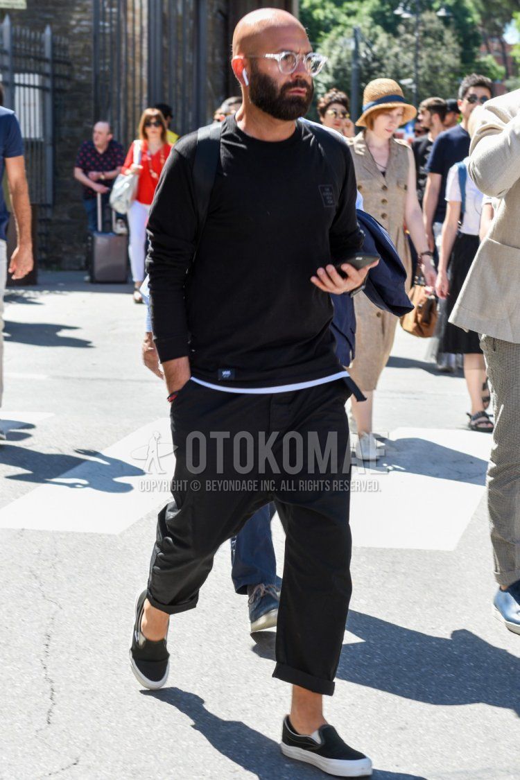 Men's spring and fall coordinate and outfit with clear plain glasses, plain black t-shirt, plain gray slacks, and black slip-on sneakers.